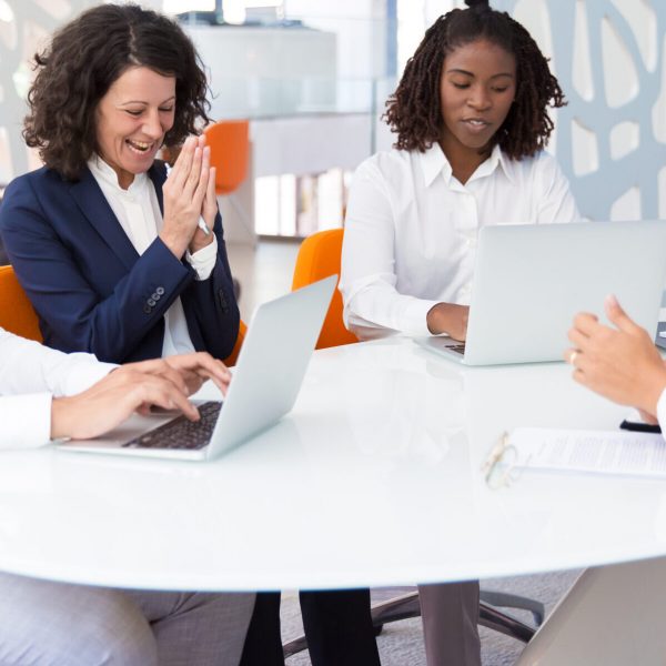 Excited business partners discussing deal. Business man and women sitting at meeting table, using laptops, talking and laughing. Meeting concept